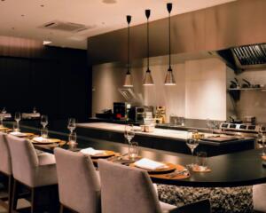 Modern restaurant chef's counter with elegant place settings and kitchen.