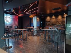 Modern bar interior with high tables, stools, and red neon lights.