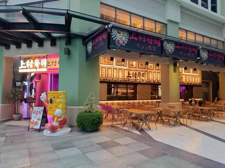 Japanese sushi restaurant exterior with outdoor seating and character statue.