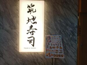 Tsukiji Sushi restaurant sign and menu board against marble wall.